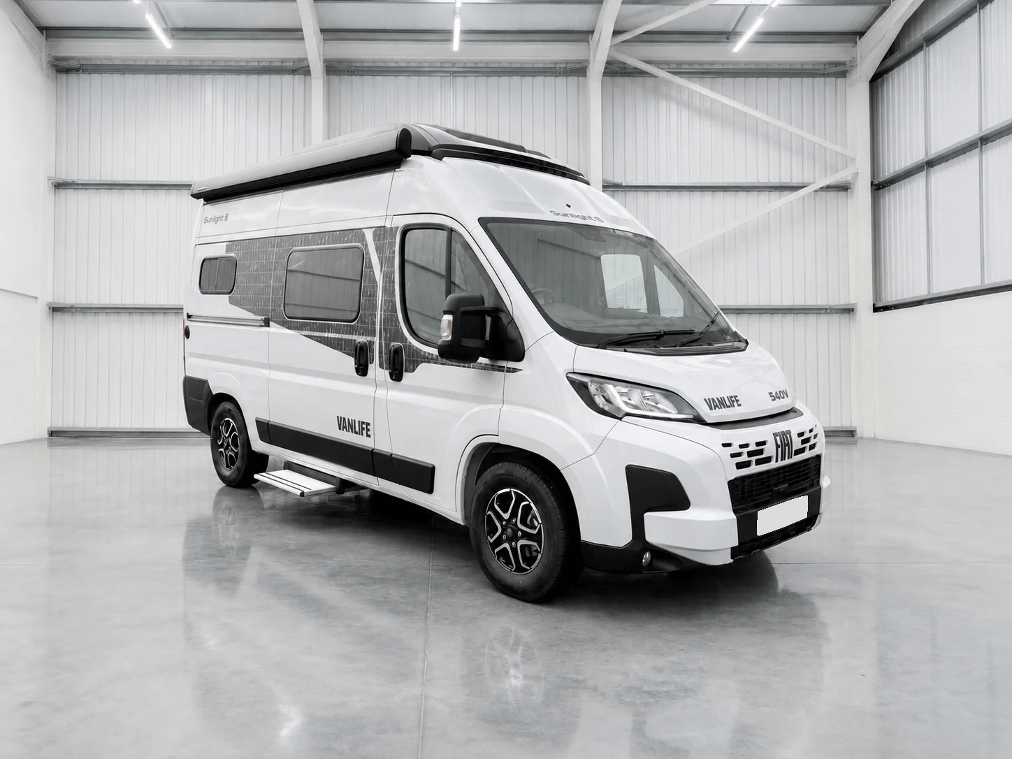 White Sunlight Vanlife campervan with roof rack parked in bright warehouse.
