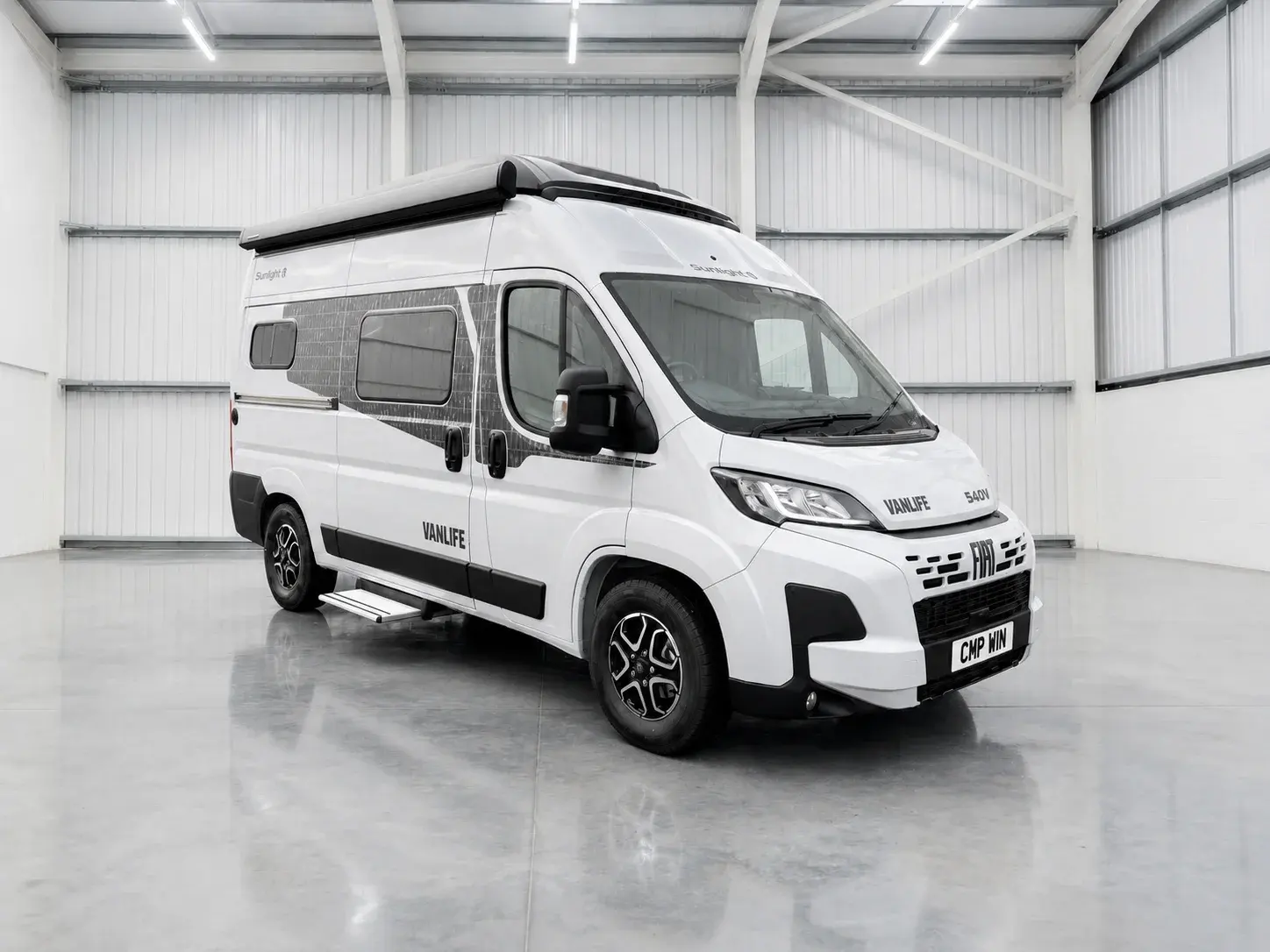 White Sunlight Vanlife campervan with roof rack parked in bright warehouse, front view with CMP WIN number plate.